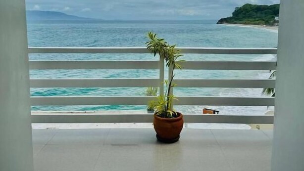A balcony with a potted plant, overlooking a beach with clear blue waters and a distant mountain. - Playa Blanca Beach Resort & Dive Centre (Puerto Galera)