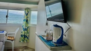 A room with a TV mounted on the wall, a small table with a kettle, a chair, and a window with a view of the sea. - Playa Blanca Beach Resort & Dive Centre (Puerto Galera)