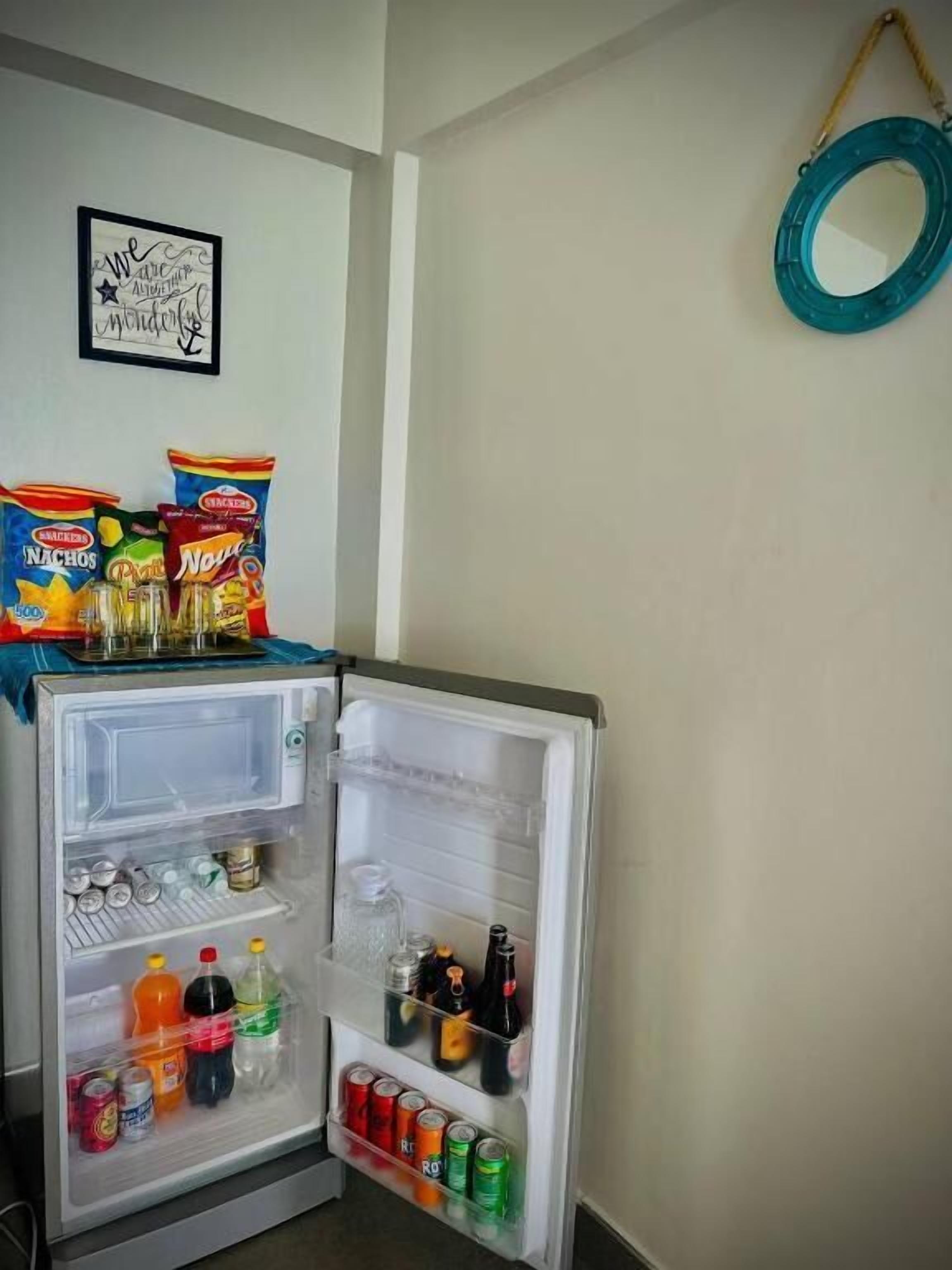 A small, open refrigerator stocked with snacks and drinks, a framed quote on the wall, and a blue circular object hanging on the wall.