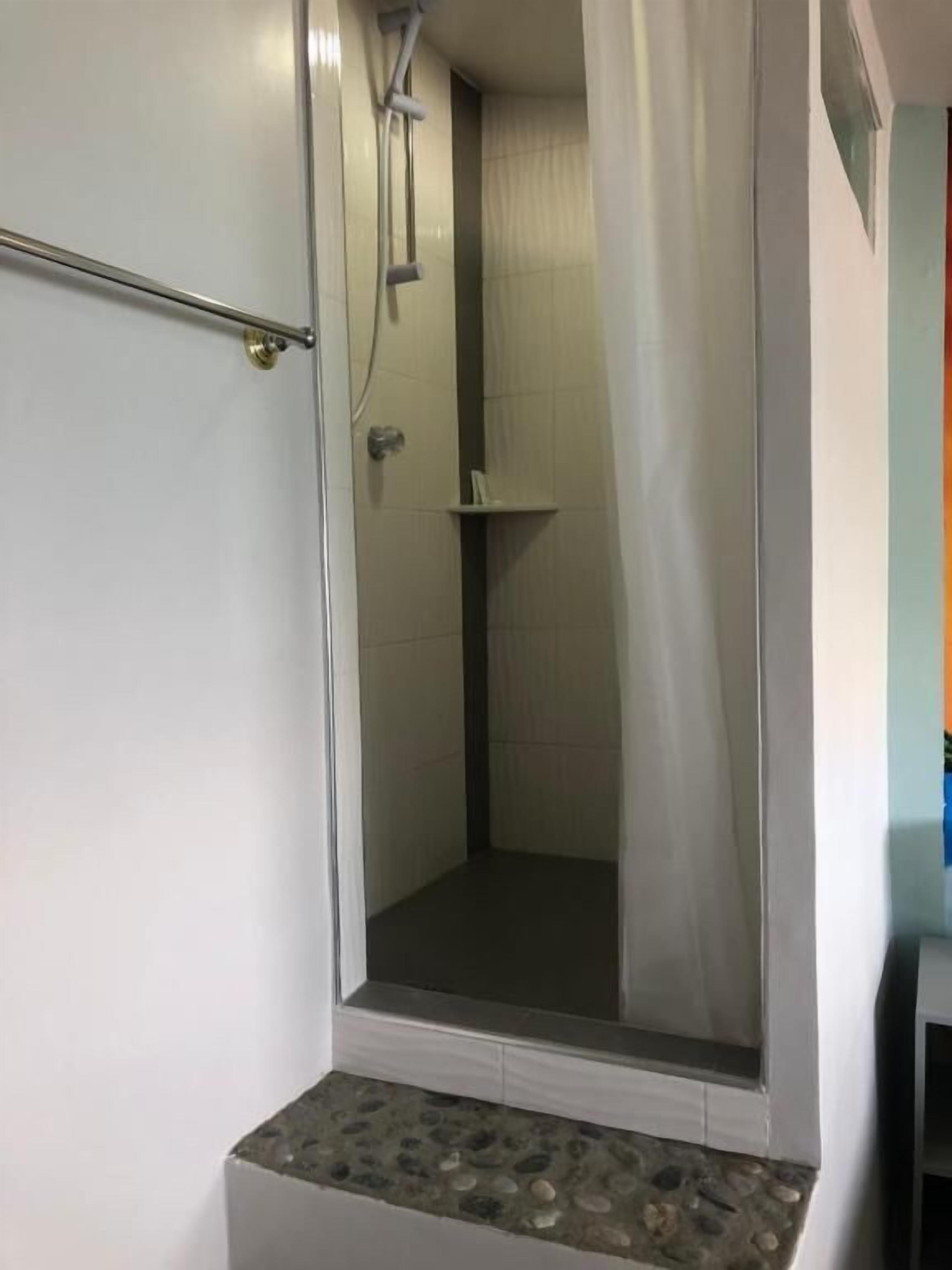 A small, enclosed shower area with a glass door, a metal grab bar, and a tiled floor.