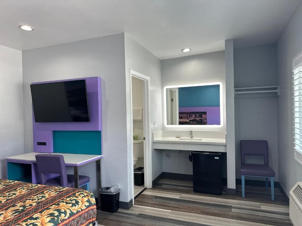 Une chambre d’hôtel de taille réduite, comprenant un lit, un bureau, une télévision, un miroir et une petite kitchenette.