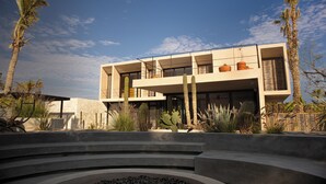 Un bâtiment moderne doté d’un toit plat, de grandes fenêtres et d’une cour intérieure agrémentée de cactus et de palmiers.