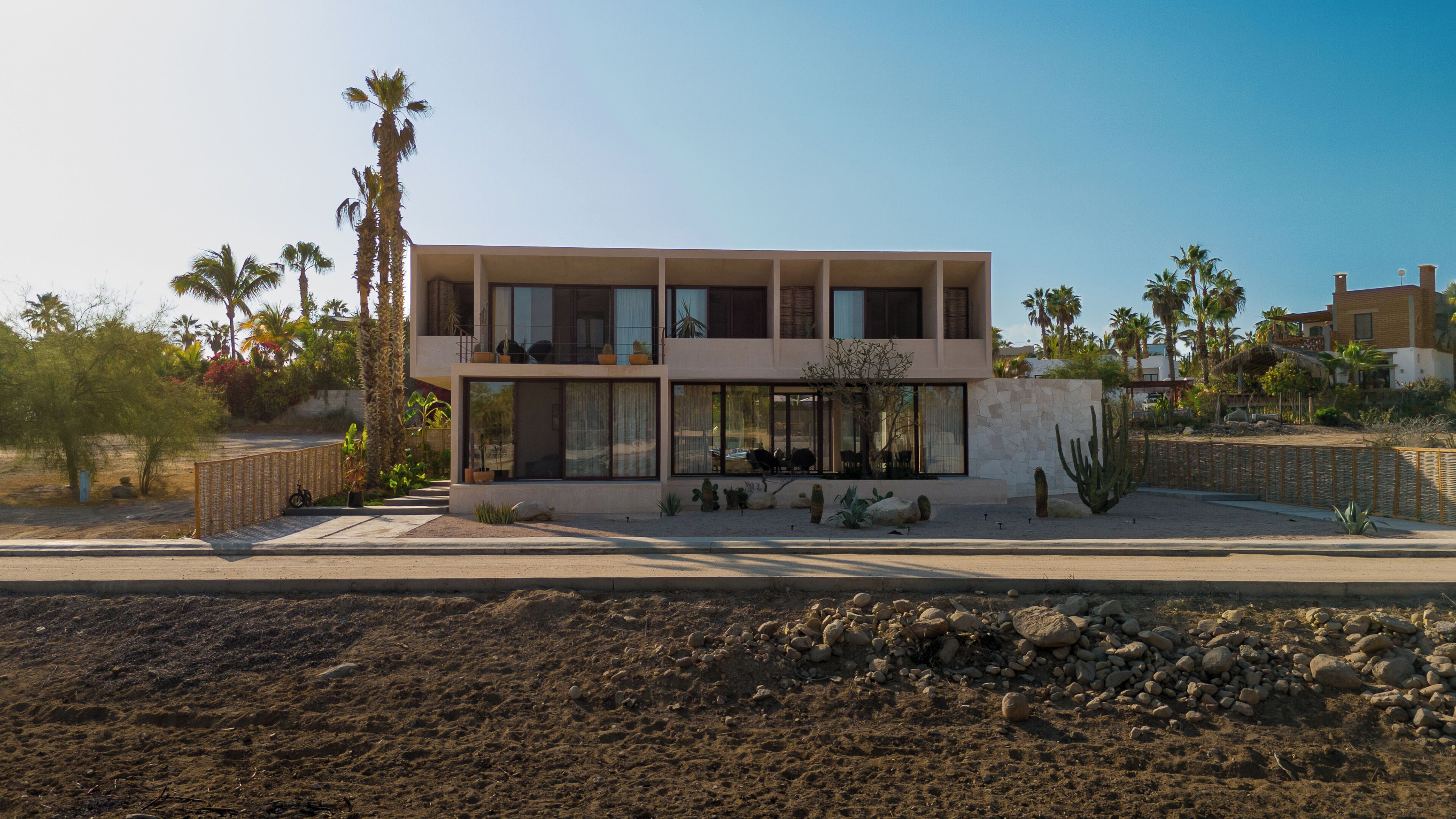 Une maison moderne à deux étages, dotée de grandes fenêtres, d’un balcon et surplombant un paysage désertique.