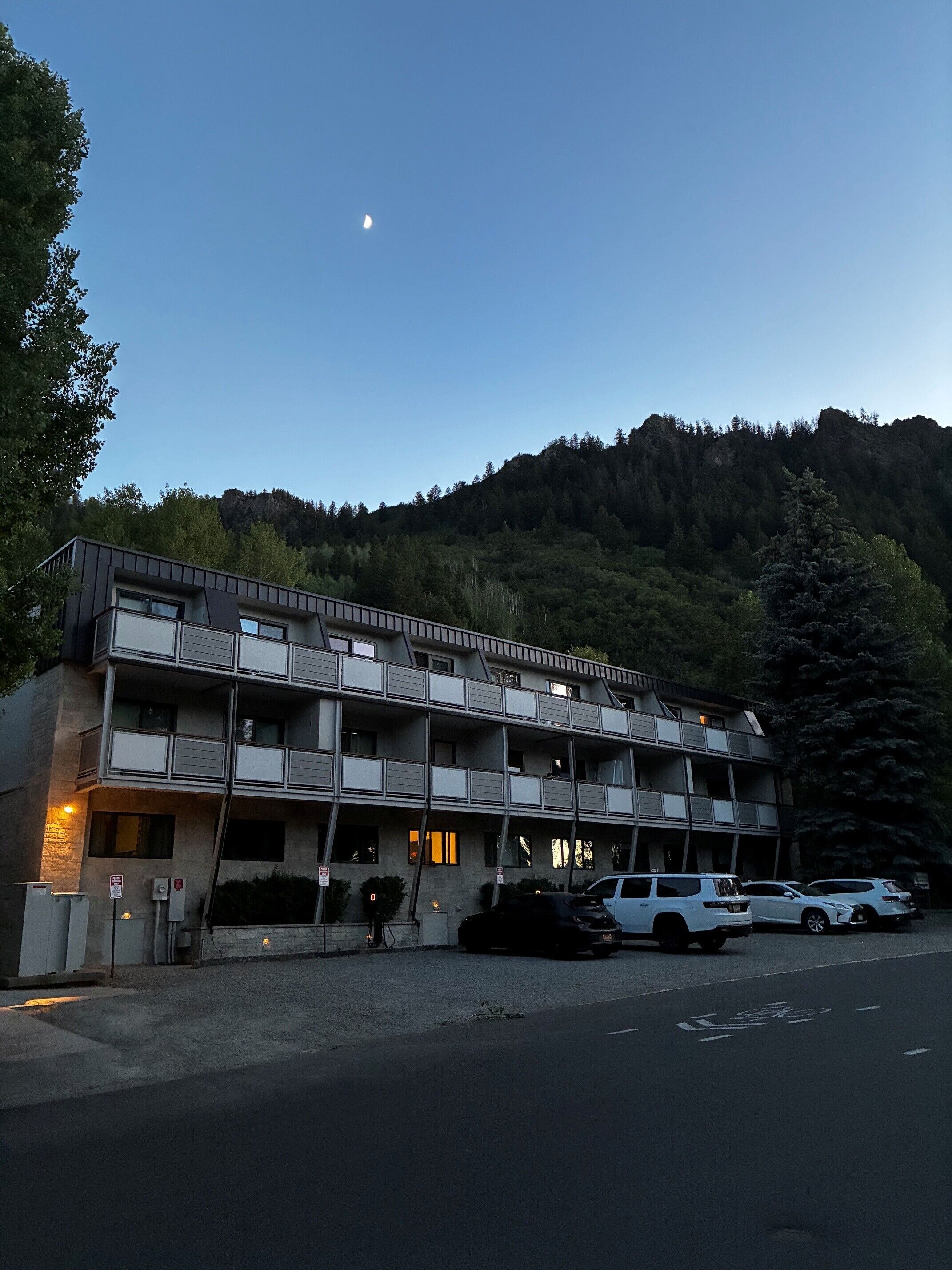 Ein mehrstöckiges Motel mit Balkonen, einem Parkplatz und einem bewaldeten Hügel im Hintergrund.