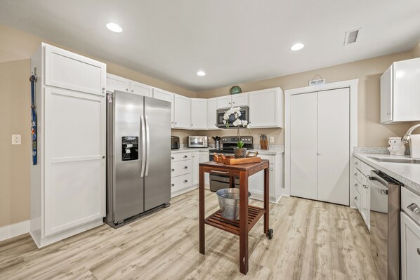 A modern kitchen with white cabinetry, stainless steel appliances, and a wooden table with a metal bucket.