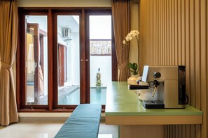 Een kamer met een schuifglasdeur naar een balkon, een koffieapparaat op een groen aanrecht en een bank.