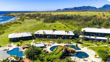 A resort with multiple buildings, a large pool area, and a view of the ocean and mountains.