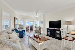 Ein geräumiges Wohnzimmer mit großem Fernseher, einem Essbereich mit Tisch und Stühlen sowie einer Sitzecke mit Sofa und Sesseln.