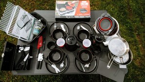 Un campamento equipado con una parrilla portátil, utensilios de cocina y una mesa lista para una comida.