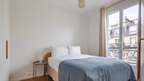 Une chambre à coucher avec un lit, une table de chevet et une vue sur les immeubles par la fenêtre.