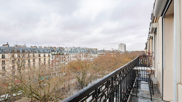 Un balcon offrant une vue sur le paysage urbain, avec des bâtiments et des arbres.