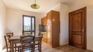 Uma sala de jantar com mesa e cadeiras de madeira, uma cozinha com armários de madeira, e uma porta grande de madeira.