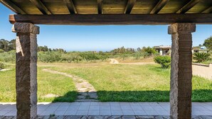 A stone-paved patio with a pergola overhead, leading to a grassy area with a path. - Lovely apartment for 5 people with WIFI, TV, terrace and pets allowed (Siniscola)