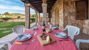 An outdoor dining area with stone walls, a red tablecloth, and white chairs. - Lovely apartment for 5 people with WIFI, TV, terrace and pets allowed (Siniscola)
