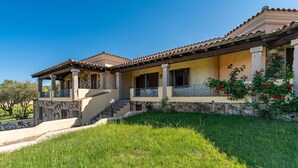 Une maison à deux étages avec une façade en pierre, un toit en tuiles et un porche couvert doté d’une balustrade.