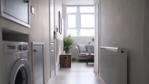 A laundry room with a washing machine, a radiator, and a window with a view of a living room. - Brand New, Beautifully Designed Apartment in the Heart of Fulham (London)
