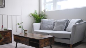 A modern living room with a grey sofa, a wooden coffee table, and a potted plant. - Brand New, Beautifully Designed Apartment in the Heart of Fulham (London)