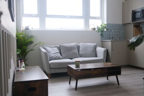 A modern living room with a grey sofa, a wooden coffee table, and a potted plant. - Brand New, Beautifully Designed Apartment in the Heart of Fulham (London)