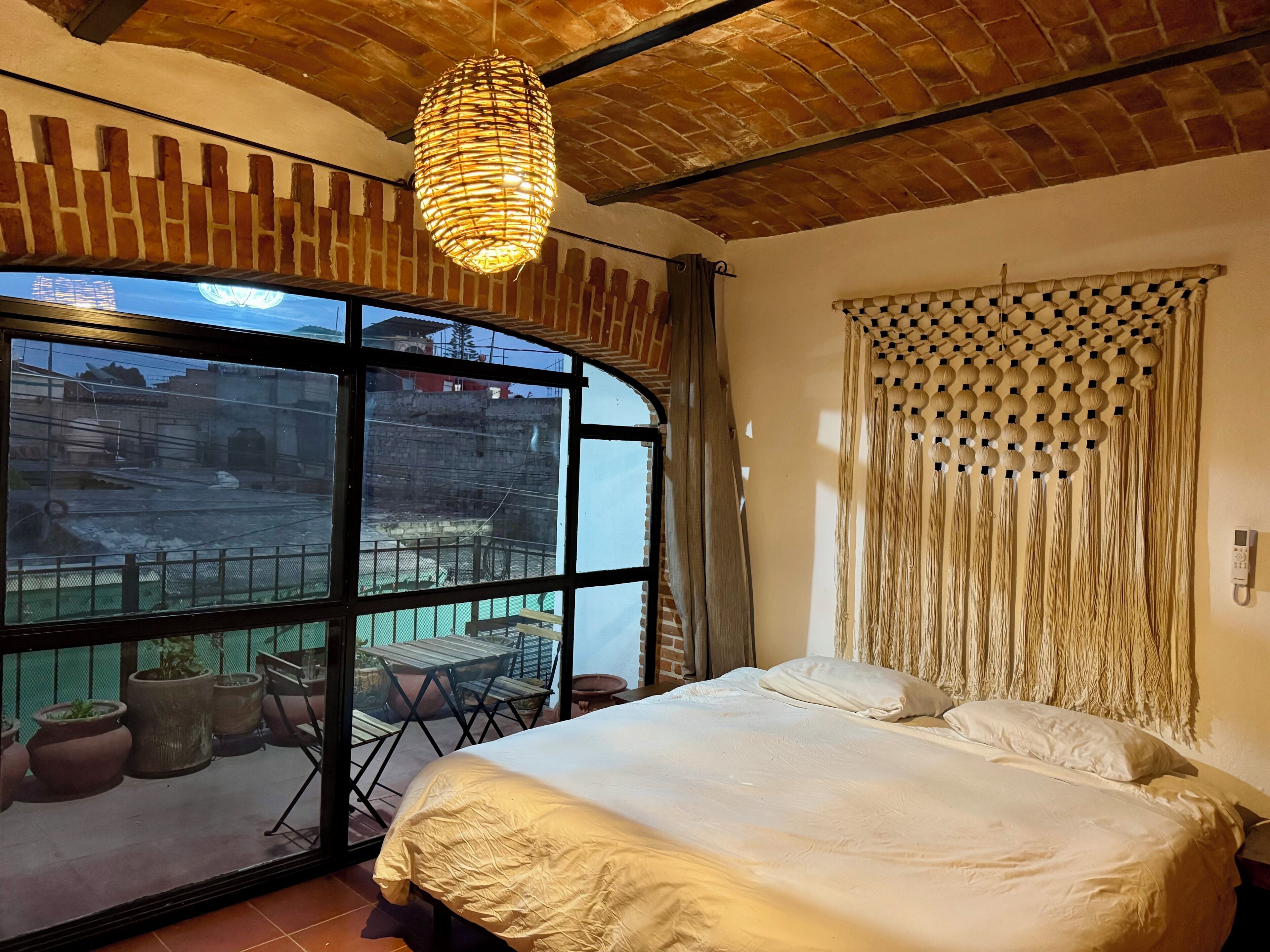 Un dormitorio con una ventana grande, una cama, una lámpara colgante y vistas al exterior.