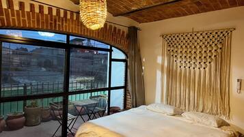 Un dormitorio con una ventana grande, una cama, una lámpara colgante y vistas al exterior.
