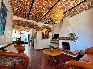 Amplia sala de estar con techo de ladrillo, chimenea, sofás de cuero, una mesa redonda de madera y un televisor.