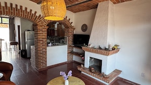 A living room with a fireplace, a dining area, and a kitchen visible through an archway.