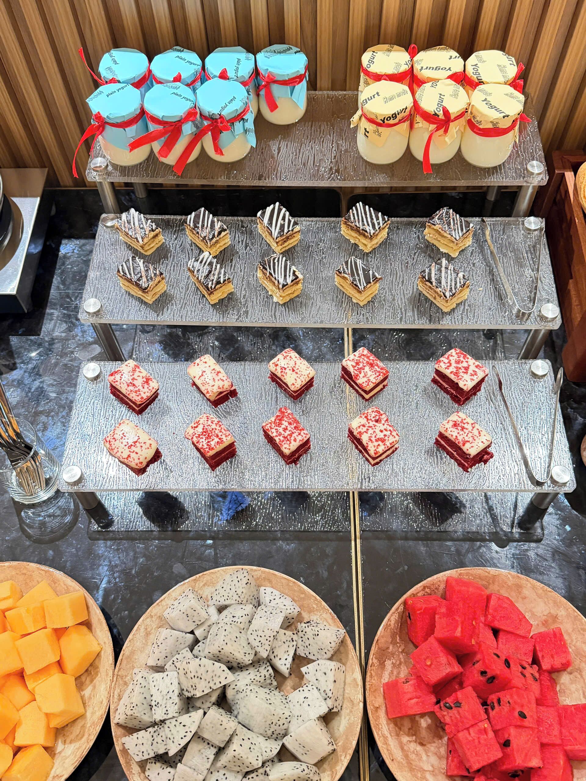 Ein Buffet mit Joghurtbechern, Desserts und Obstplatten.