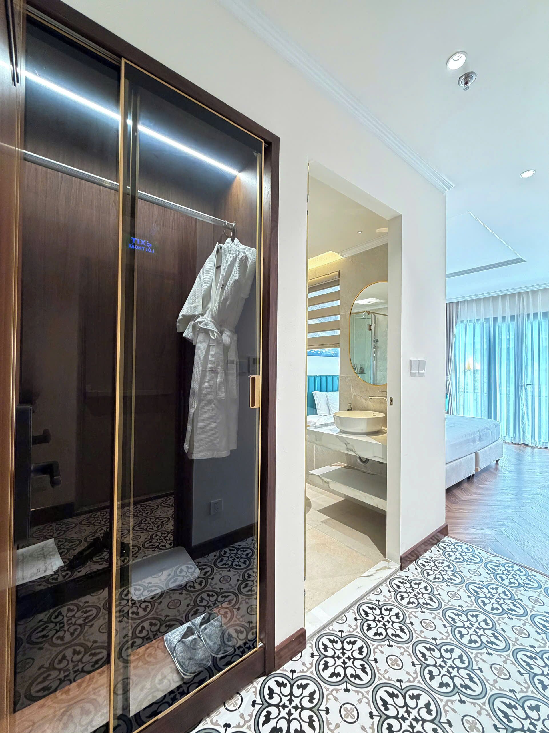 A hotel room with a walk-in closet, a bathroom with a large mirror, and a patterned floor.