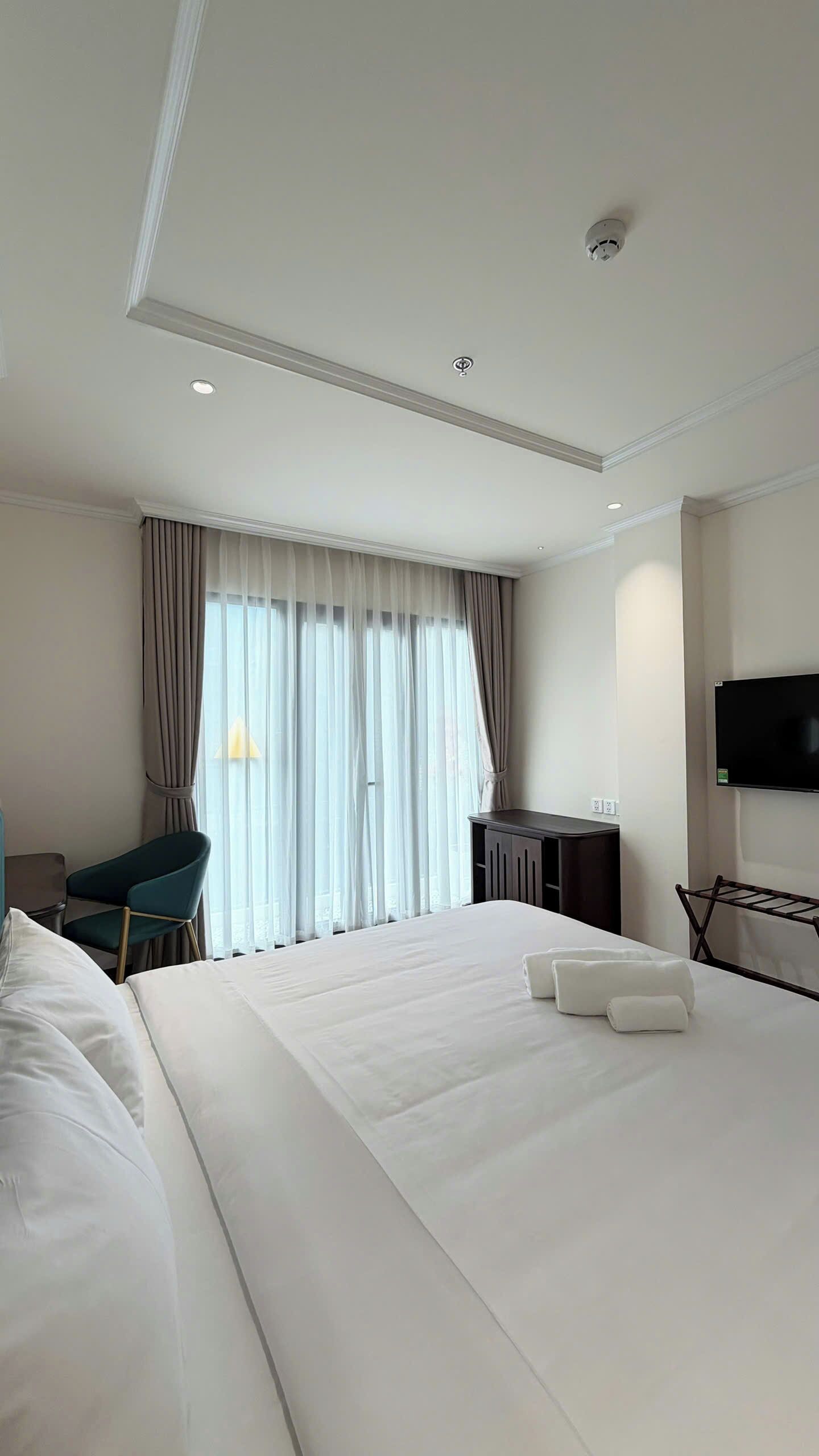 Ein Hotelzimmer mit einem großen Bett, einem Schreibtisch, einem Sessel, einem Fernseher und einem Fenster mit Vorhängen.