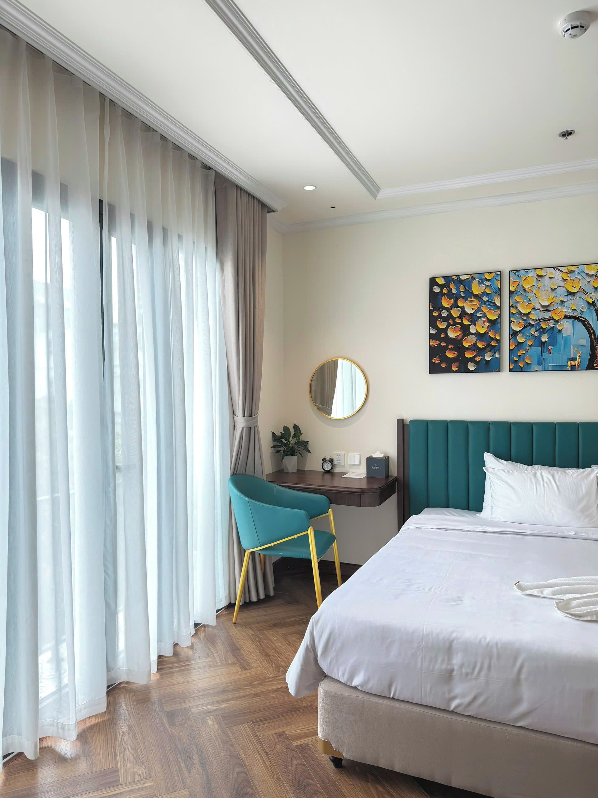 Habitación de hotel con cama, escritorio, silla, espejo y obras de arte en la pared.