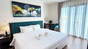 Ein Hotelzimmer mit einem großen Bett, einem Bild an der Wand, einem Schreibtisch mit Stuhl und einem Fenster mit Vorhängen.