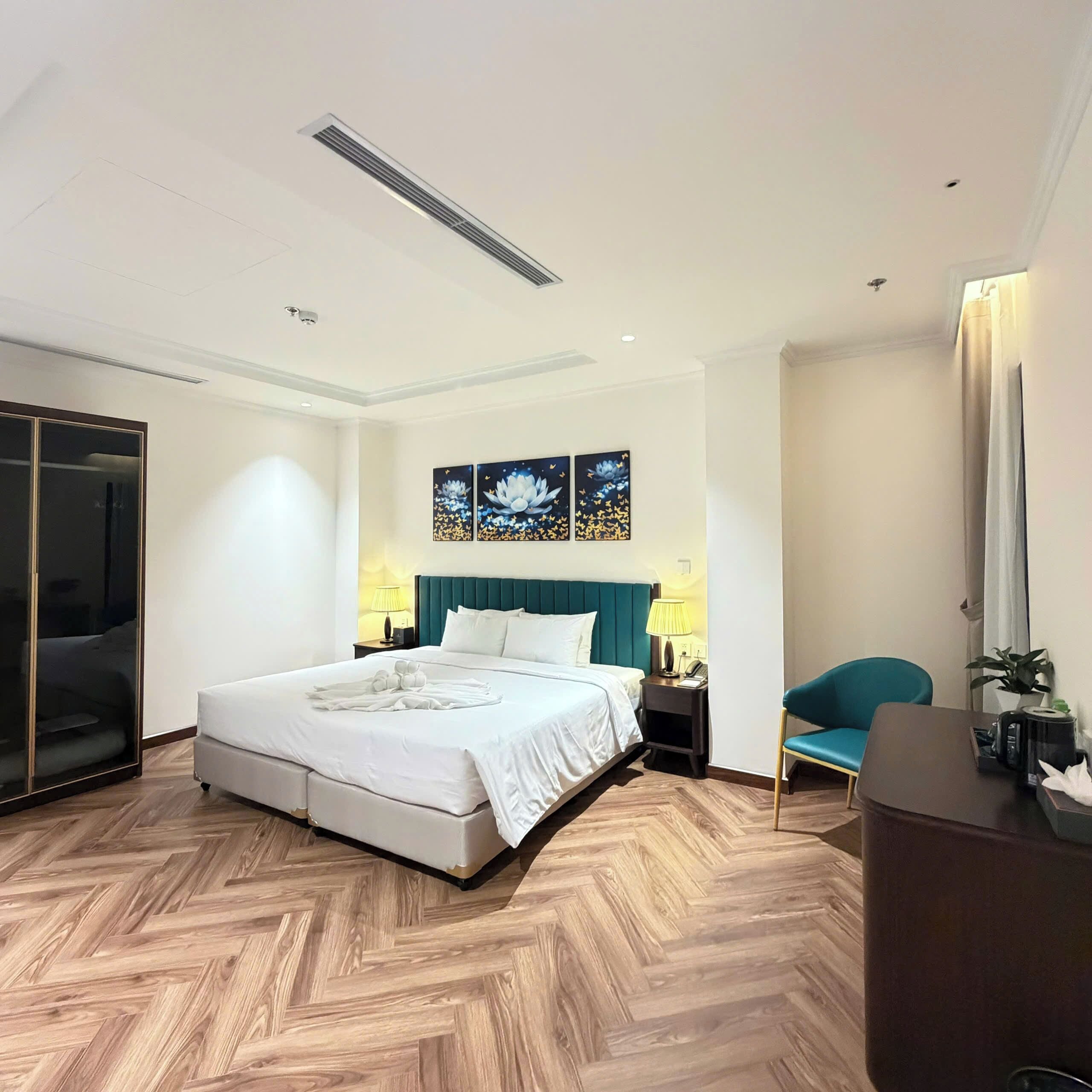 A modern hotel room with a large bed, a desk, a chair, and a wardrobe.