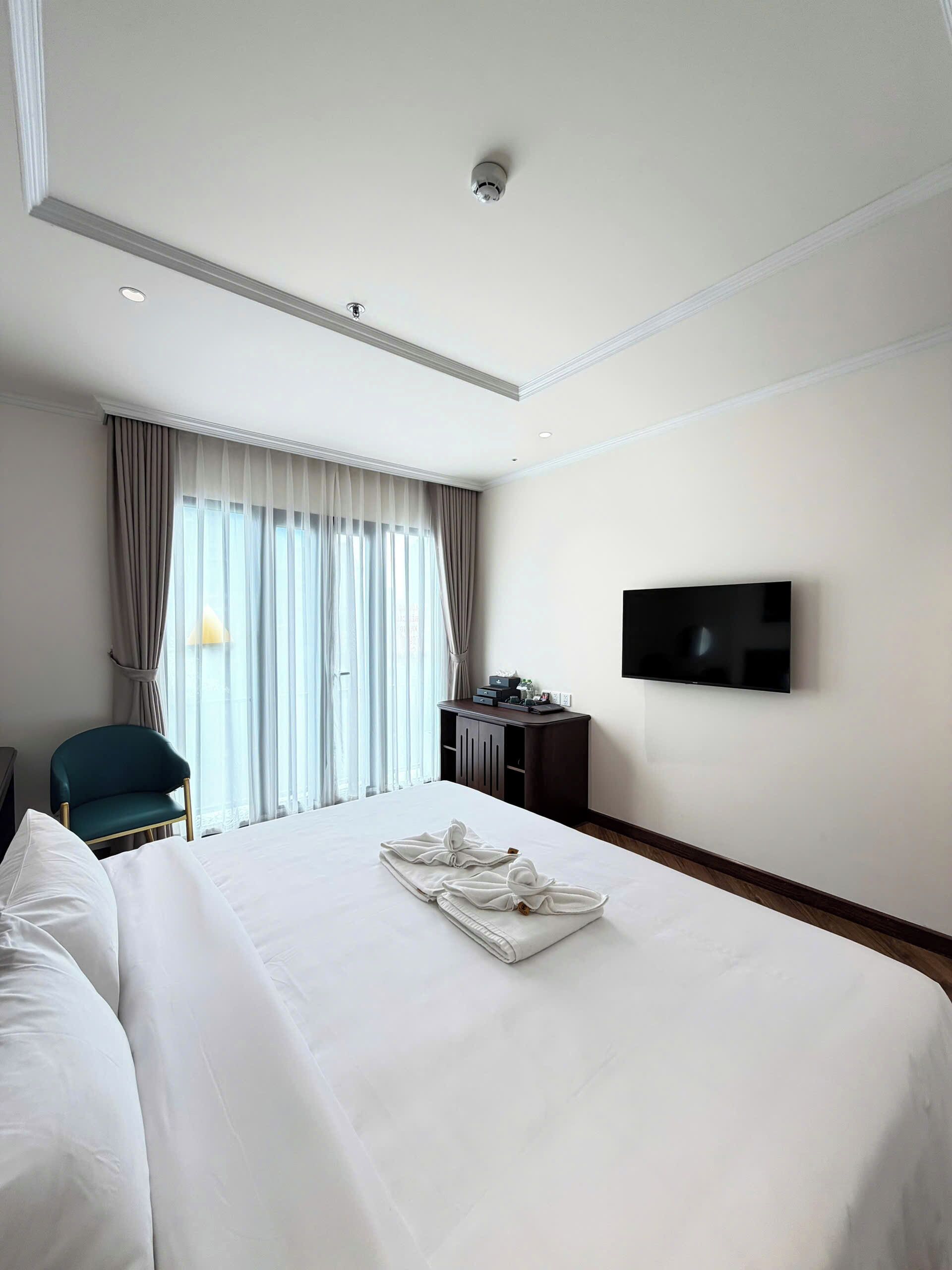 A hotel room with a bed, a desk, a chair, a TV, and a window with curtains.