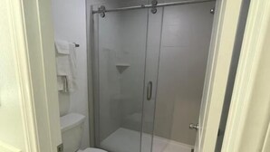 A bathroom with a toilet, a glass-enclosed shower, and a white tiled floor. - La Palma Motel - South Gate - LA area (South Gate)