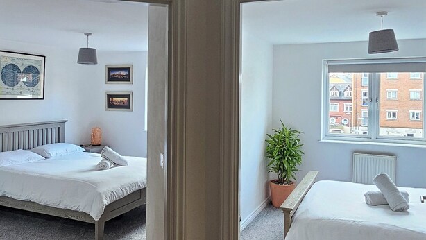 A modern bedroom with two beds, a potted plant, and a view of the city through a window.