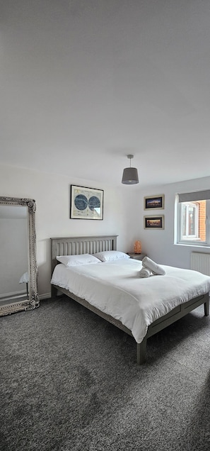 Une chambre avec un grand lit, un miroir et des tableaux encadrés accrochés au mur.