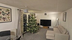 A living room with a Christmas tree, a flat-screen TV, a sofa, and a radiator.