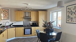 A modern kitchen with wooden cabinets, a central island with chairs, a dining table, and a large window providing natural light.