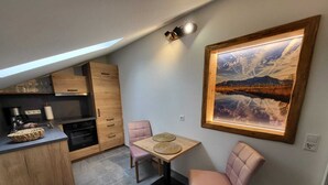 Eine kleine Küche mit Holzschränken, einem Esstisch mit zwei Stühlen und einem großen, gerahmten Landschaftsbild an der Wand.