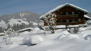 Eine Holzhütte mit geneigtem Dach, umgeben von schneebedeckten Bergen.