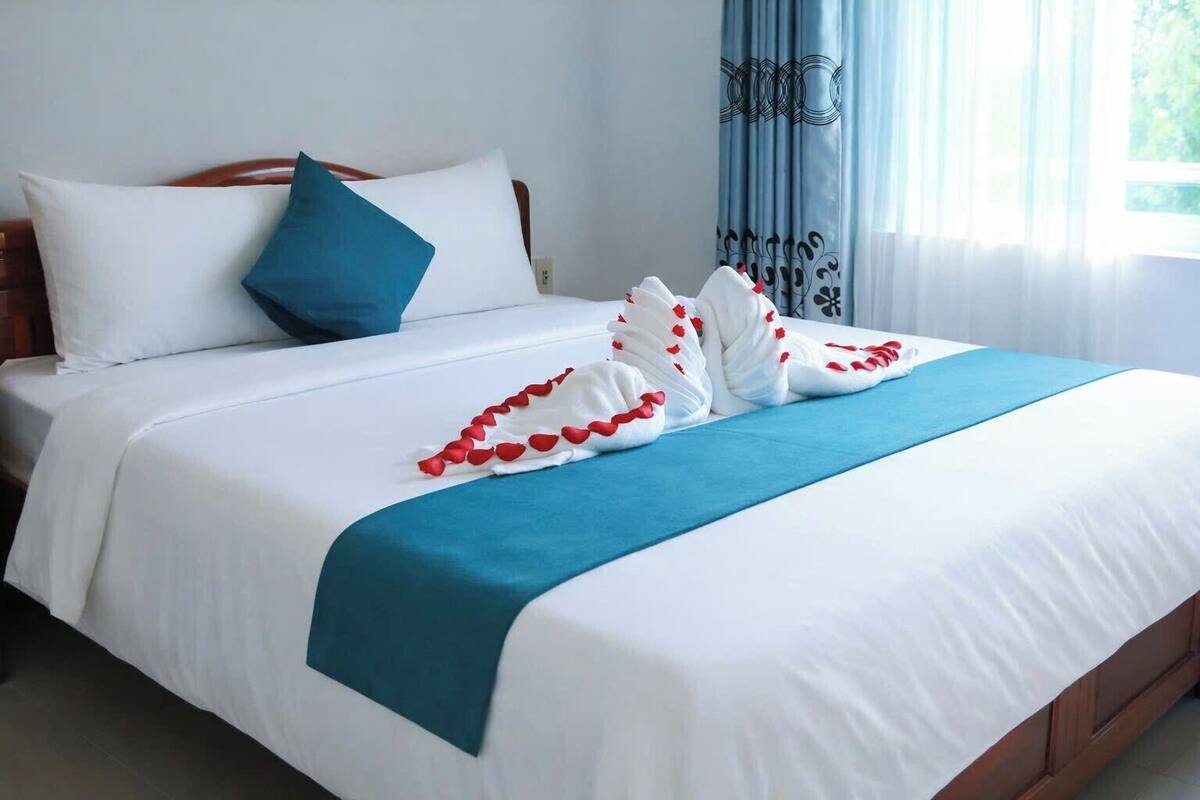 Un lit bien fait, avec une literie blanche et bleue, un oreiller bleu et une serviette décorative joliment disposée.