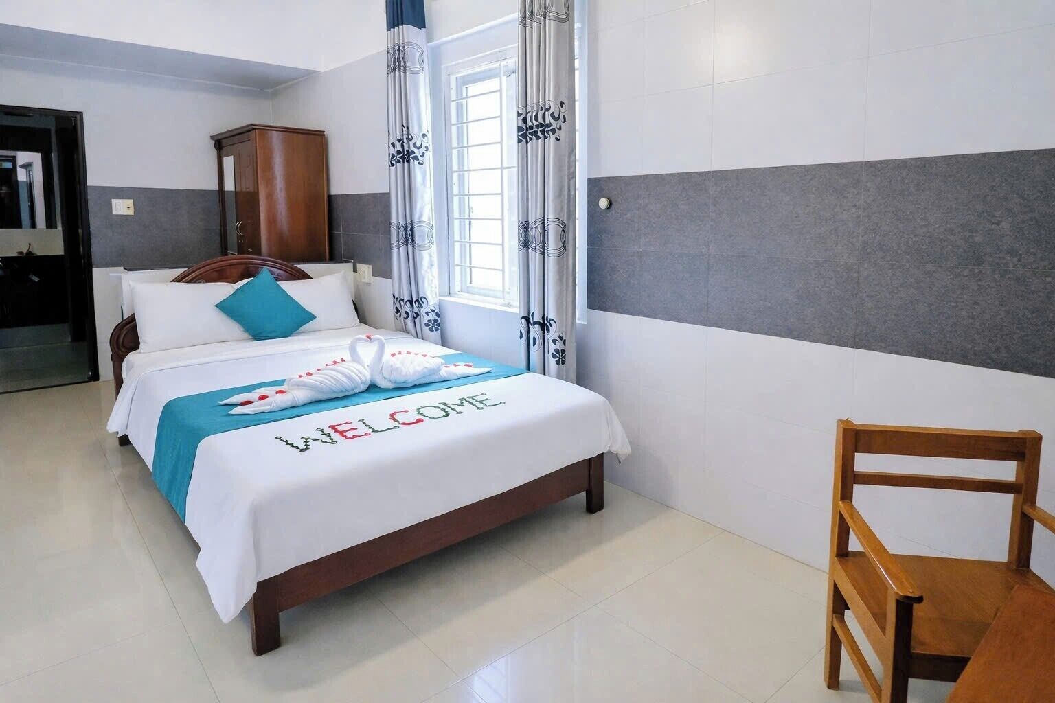 A hotel room with a bed, a wooden chair, and a wardrobe.