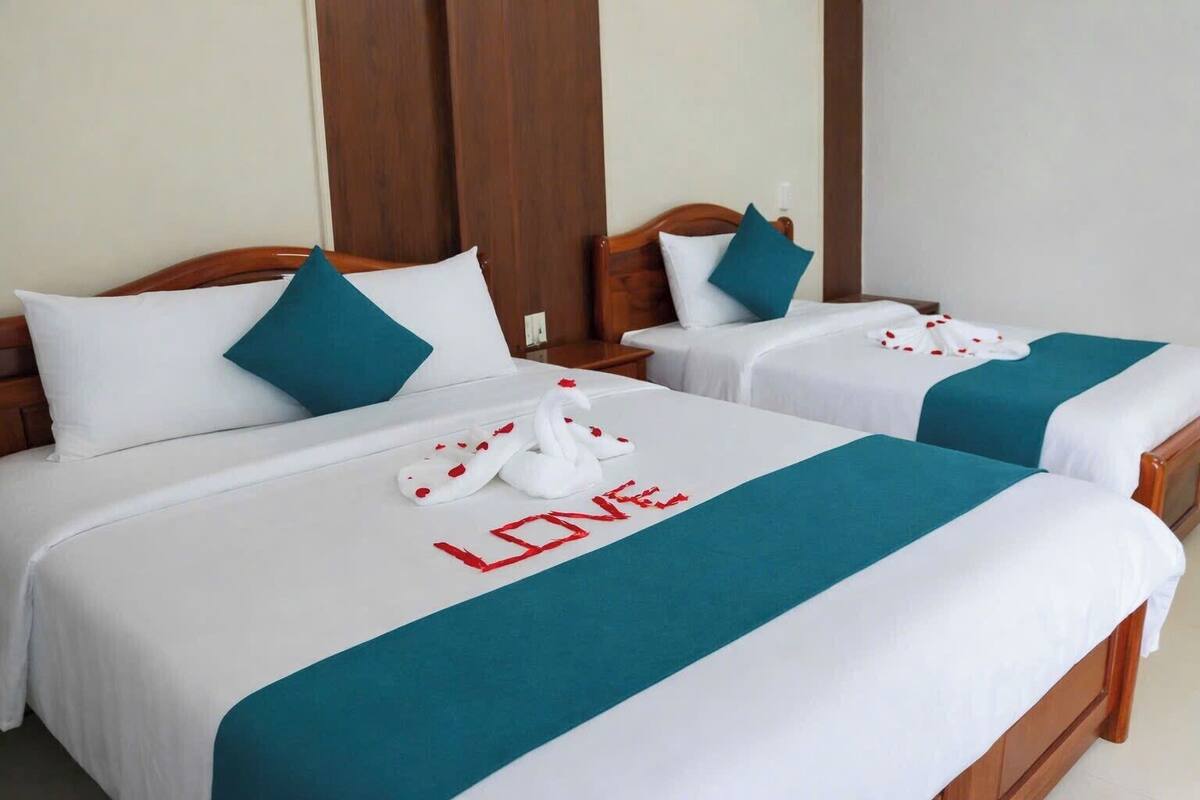 Deux lits doubles avec une literie blanche et des touches de couleur turquoise, une décoration en forme de cygne et le mot « LIVE » brodé sur la couvre-lit.