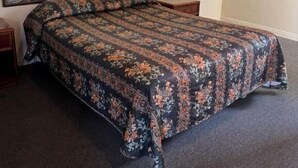 A single bed with a floral bedspread in a room with plain walls and a carpeted floor. - El Rancho Motel - Pasadena (Pasadena)
