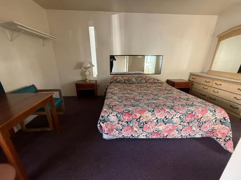 A bedroom with a bed, a desk, a chair, a dresser, a mirror, and a shelf.