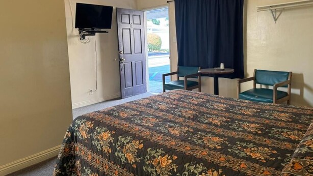 A room with a bed, a television mounted on the wall, a small table with chairs, and a door leading outside. - El Rancho Motel - Pasadena (Pasadena)