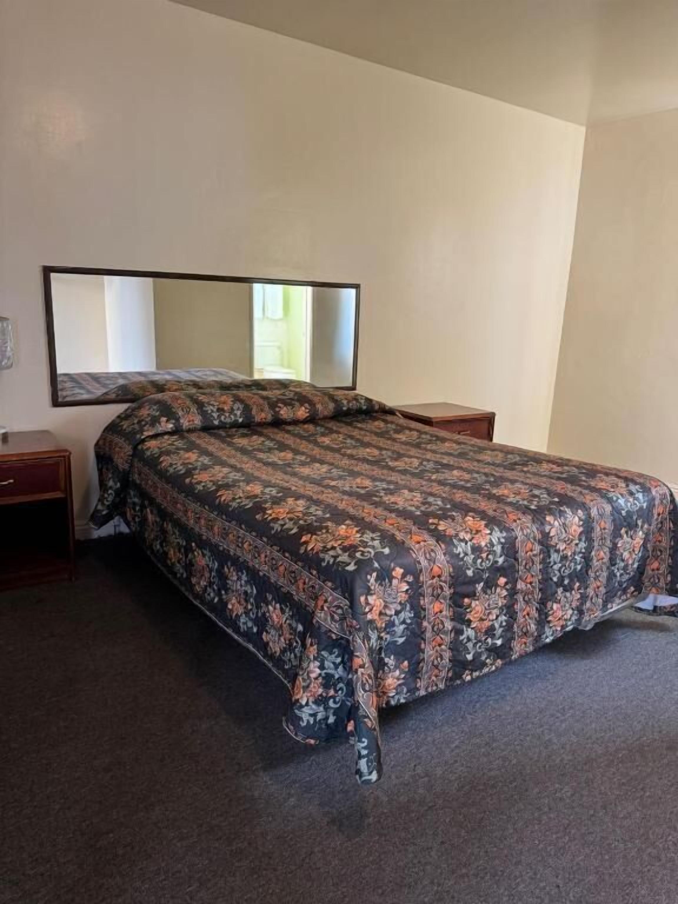 Une chambre d’hôtel standard, avec un lit simple, une table de chevet, une commode et un grand miroir au mur.
