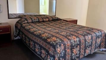Une chambre d’hôtel standard, avec un lit simple, une table de chevet, une commode et un grand miroir au mur.