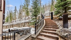 Un escalier menant à un bâtiment entouré d’un paysage enneigé et de grands arbres à feuilles persistantes.