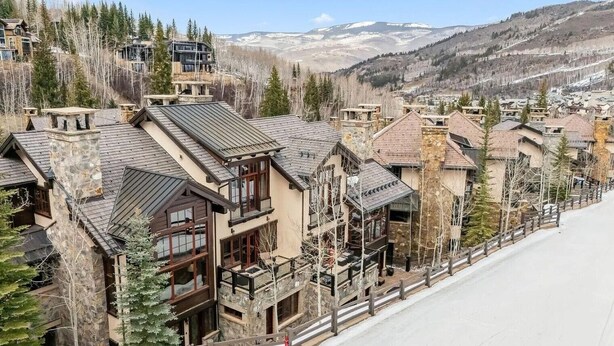 Une rangée de bâtiments en pierre et en bois, dotés de balcons, se dressant sur fond de montagnes enneigées.